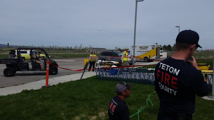 Emergency response scene with personnel, a stretcher, ambulance, and fire department vehicles.