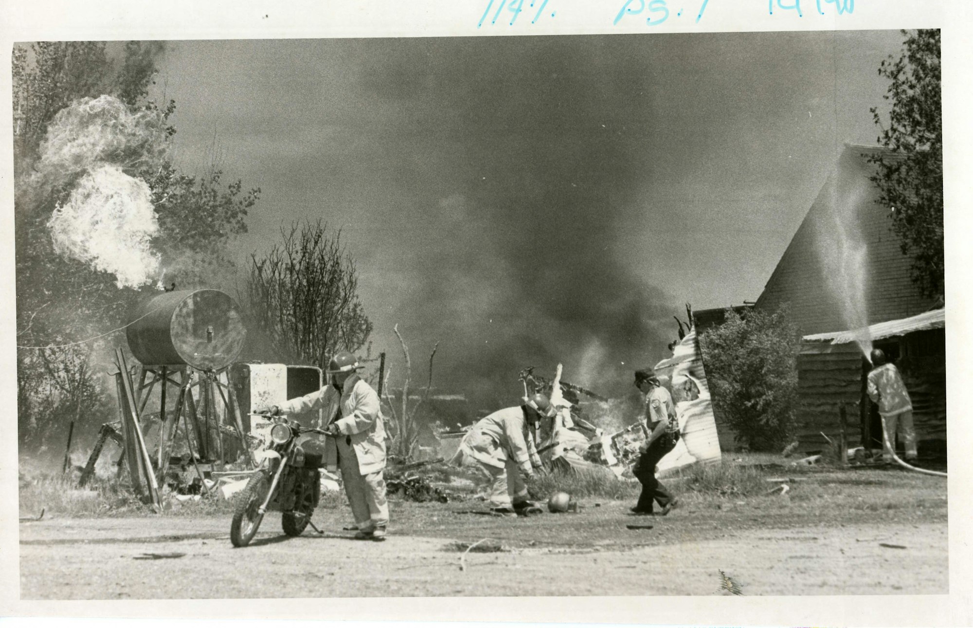 Firefighters in action, smoke, water being sprayed, damaged structures.