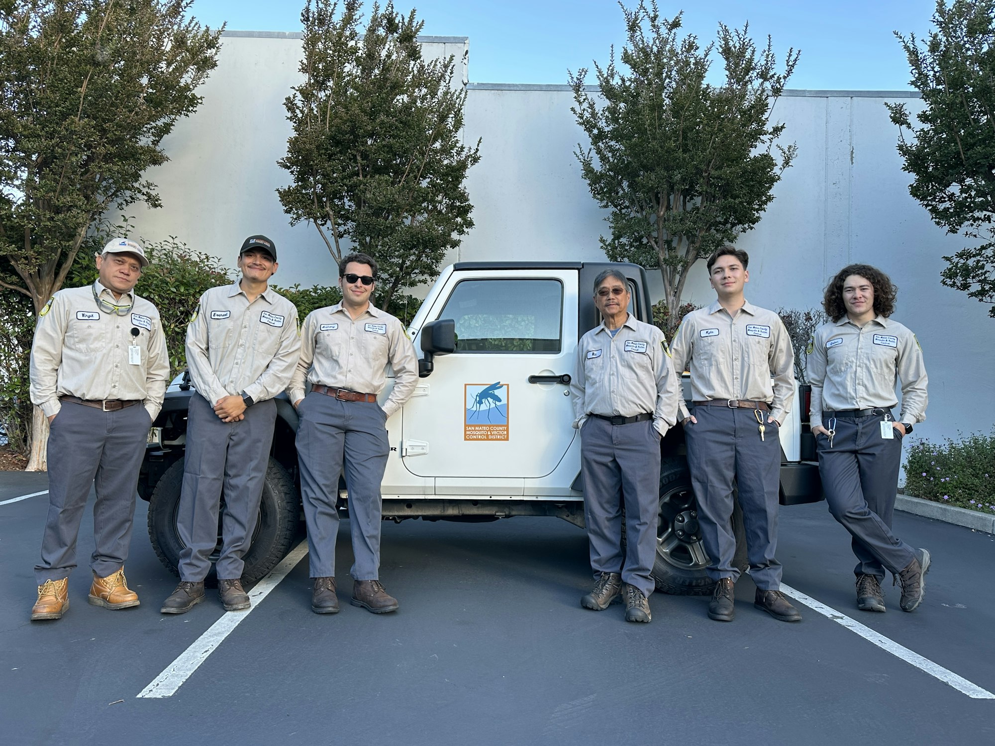 Six people in uniforms stand together in front of a white truck parked in a lot.