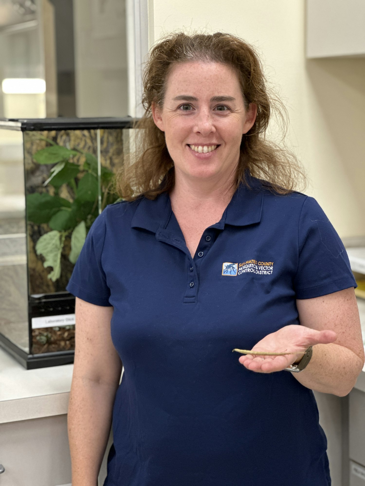 Photograph of a person smiling at the camera while holding a little thin, long object in her hand.