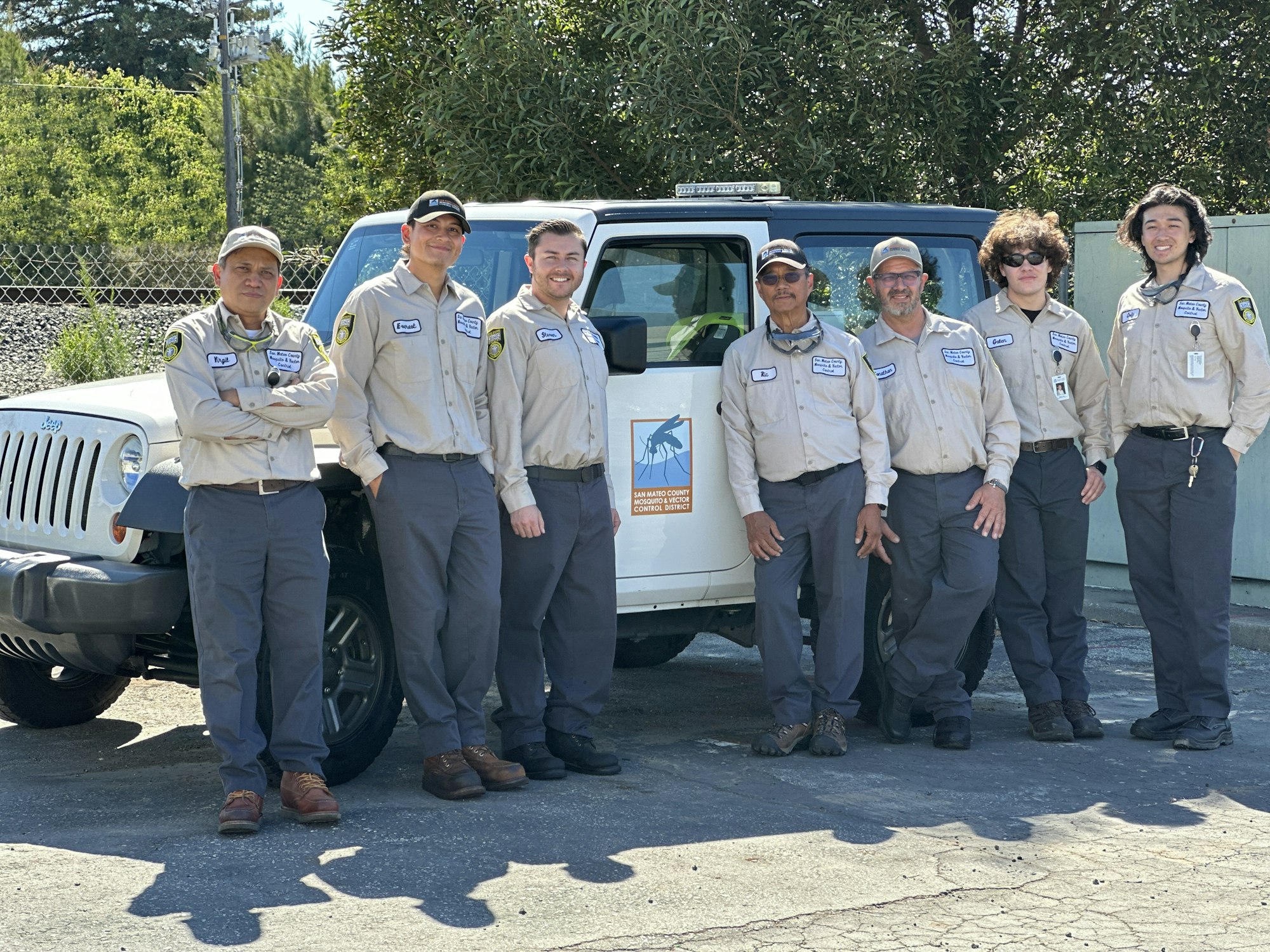 A group of seven uniformed individuals standing beside a white Jeep with a logo on the door. The logo is the San Mateo County Mosquito and Vector Control District logo.