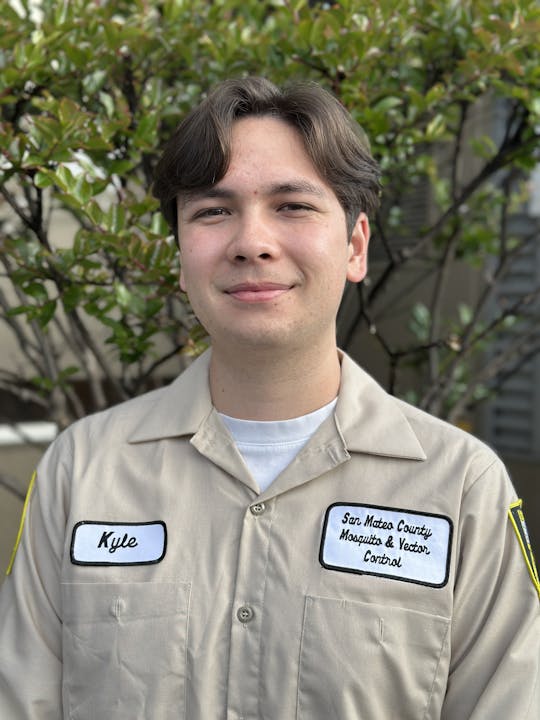 A person named Kyle wearing a uniform for San Mateo County Mosquito & Vector Control, standing outdoors.