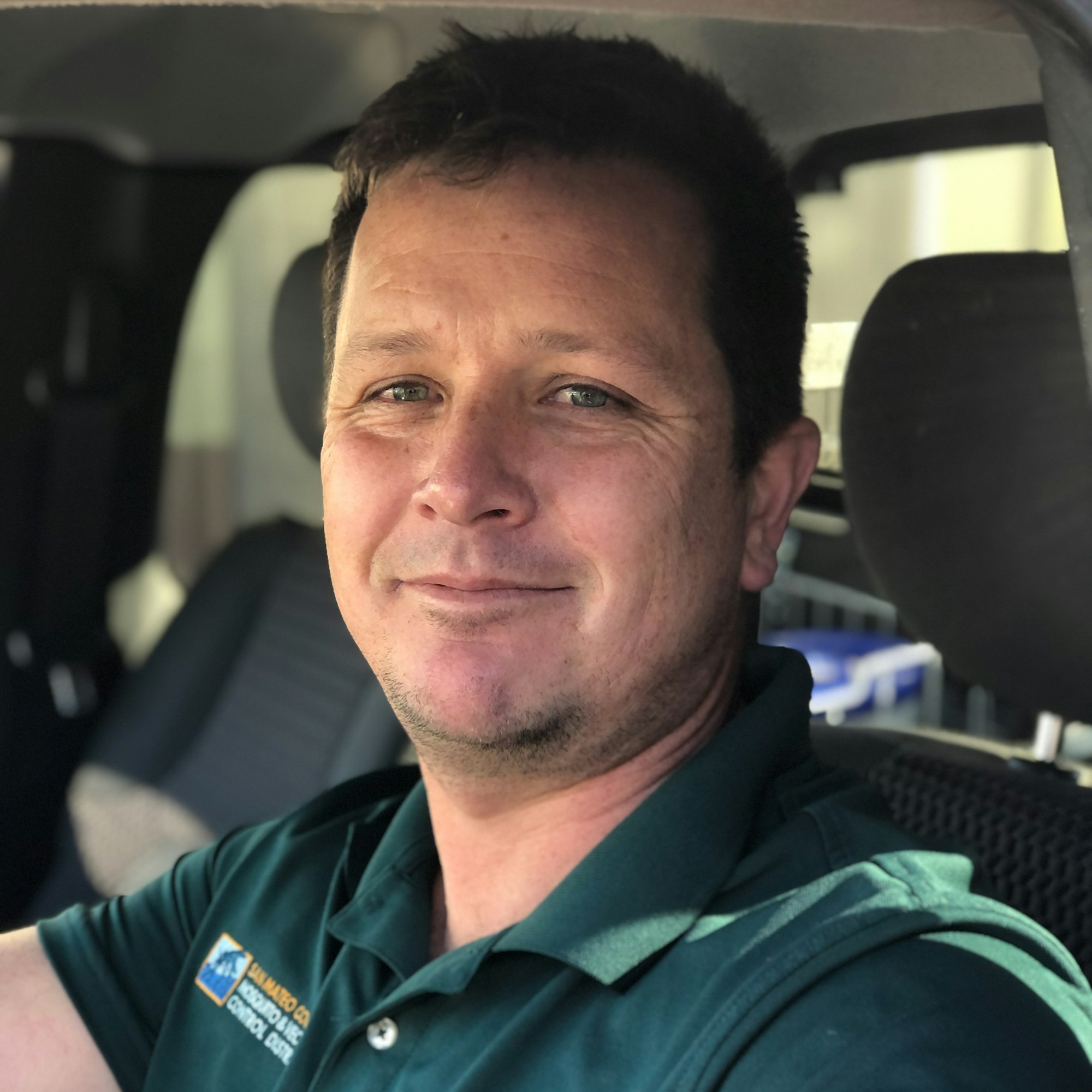 Smiling person in green shirt with District logo sitting in a vehicle