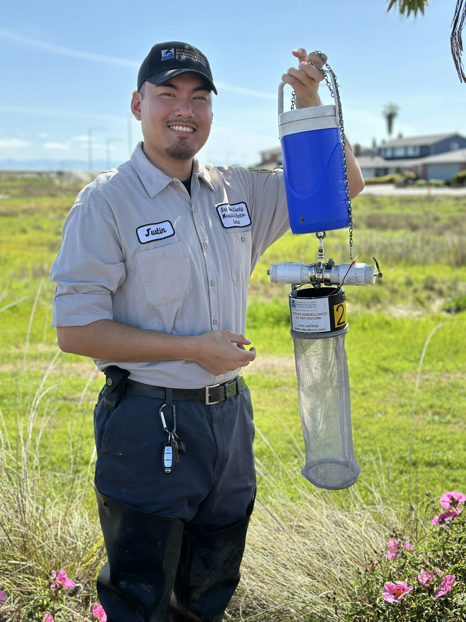 A person outdoors holding a blue and white device with a net, a kind of mosquito trap.