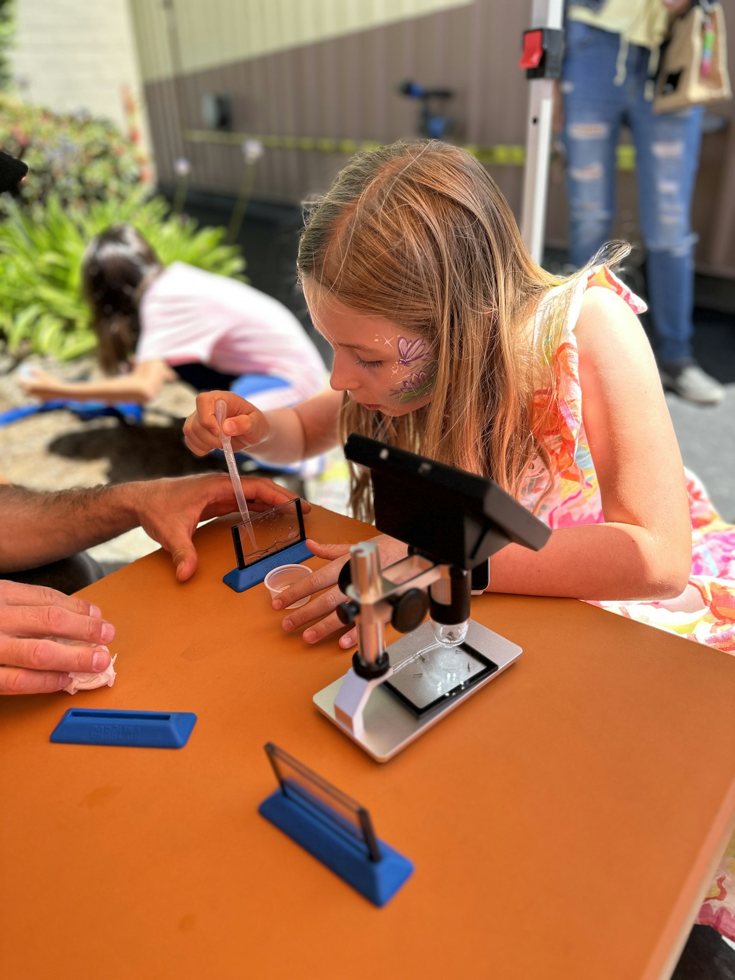 A child is using a pipette and a microscope, engaged in a science activity outdoors.
