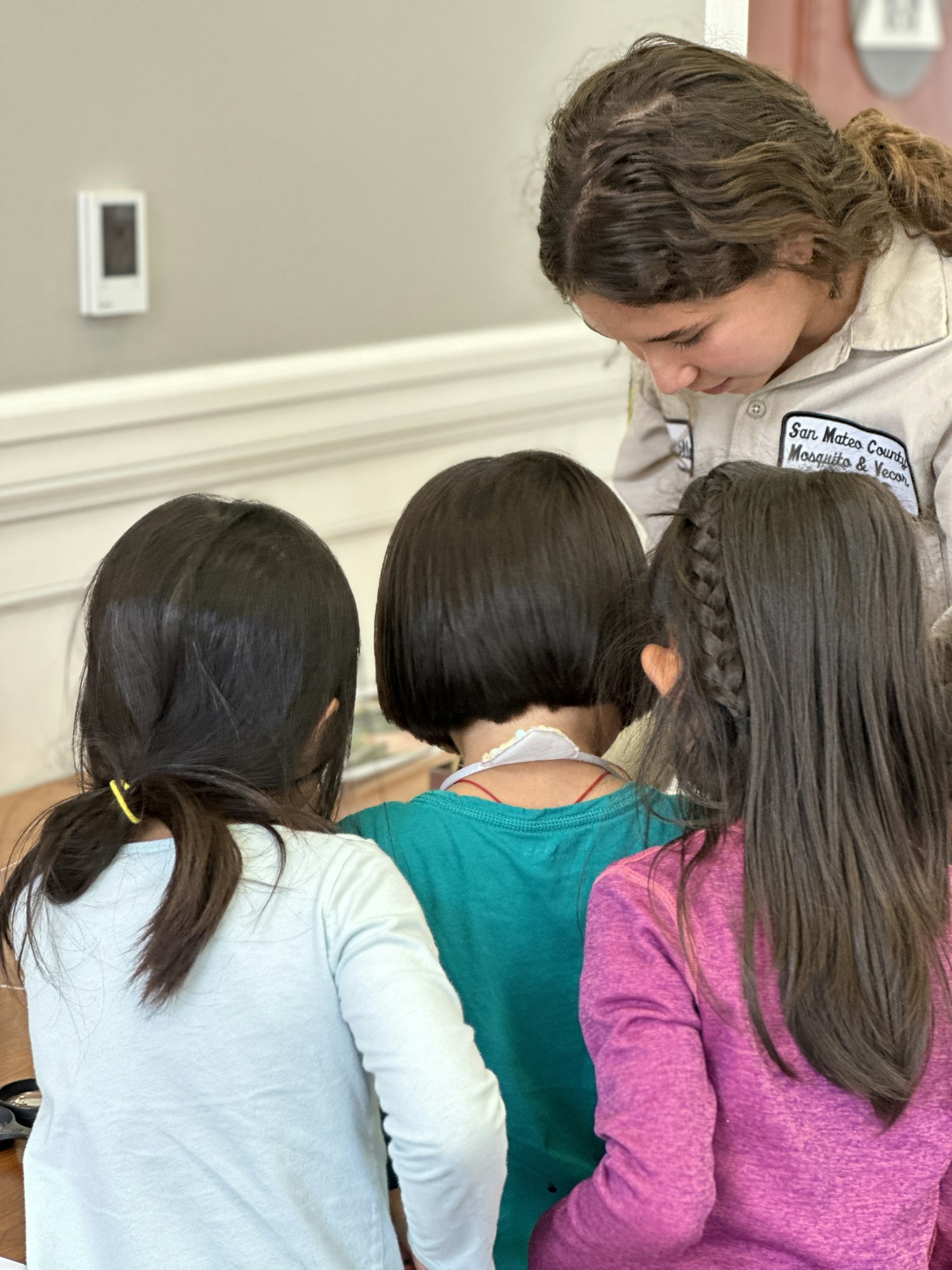 A person in uniform interacts with three children gathered around a table.