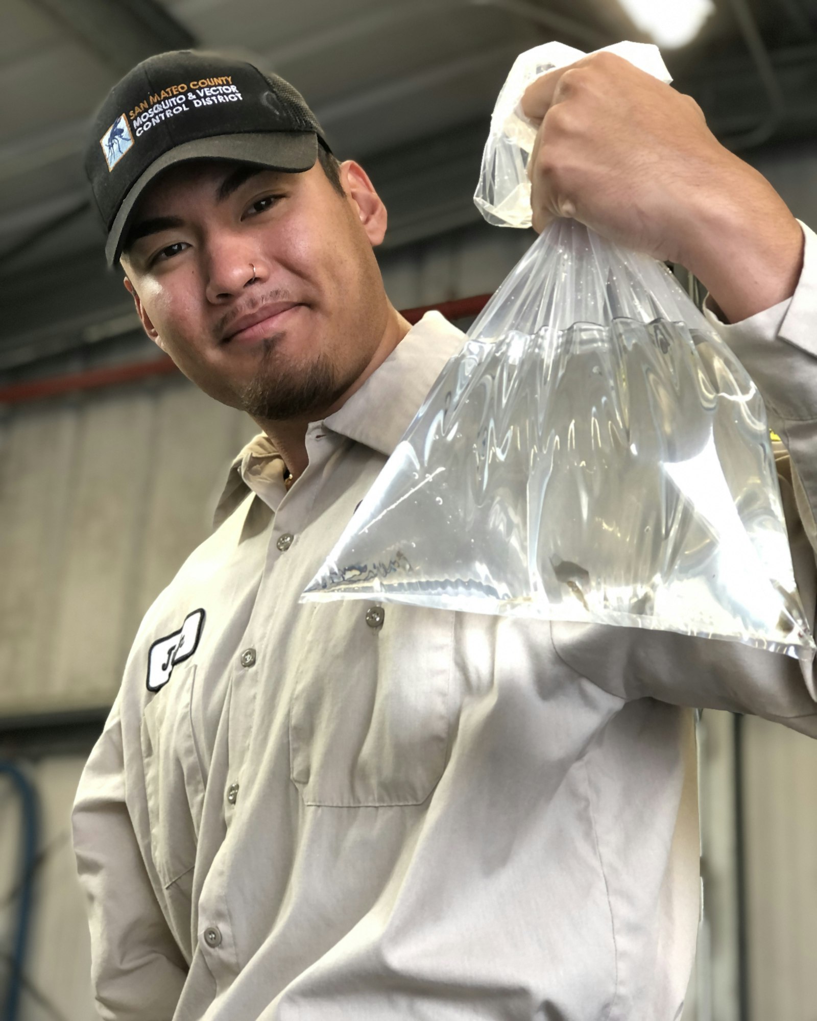 Person in black hat and tan shirt holding up a clear plastic bag with water and small fish