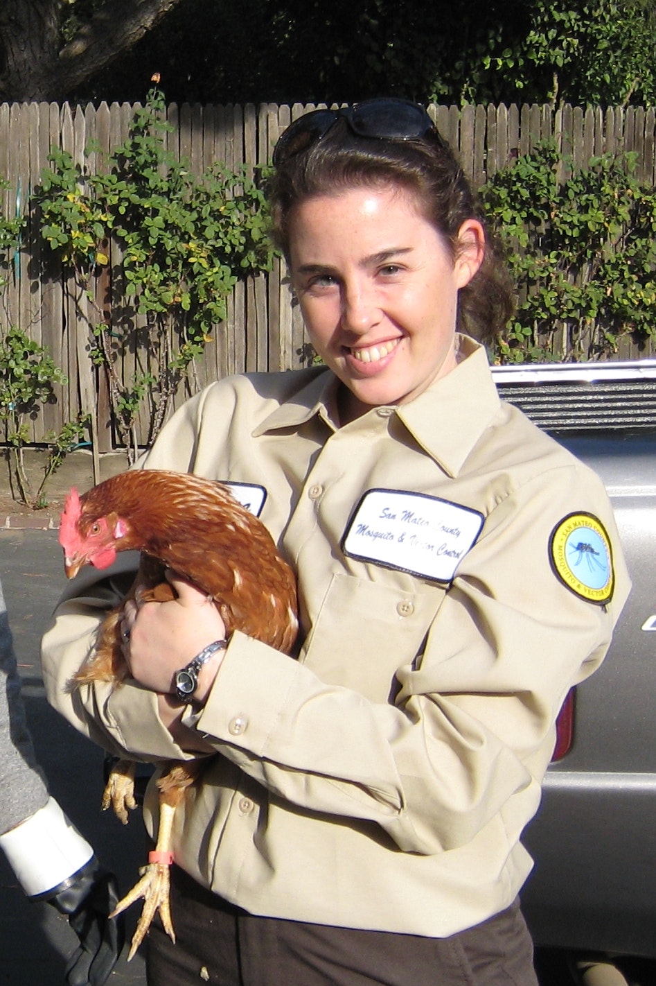 A person in a uniform smiles while holding a brown chicken.