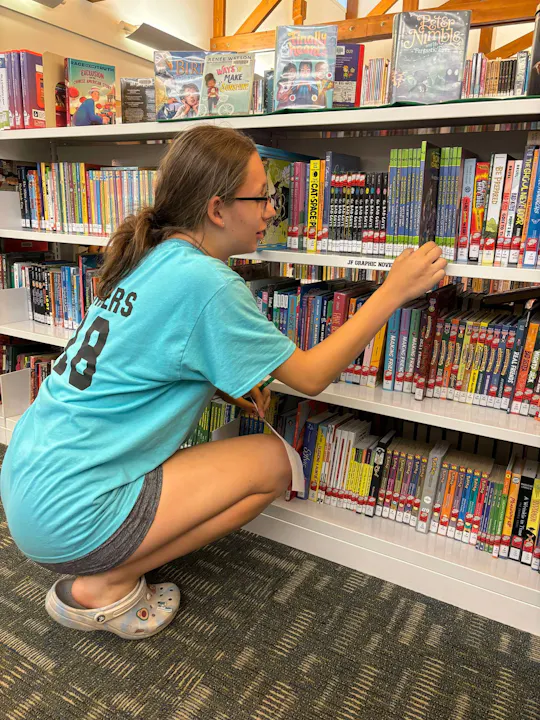A person is browsing books at a library shelf.