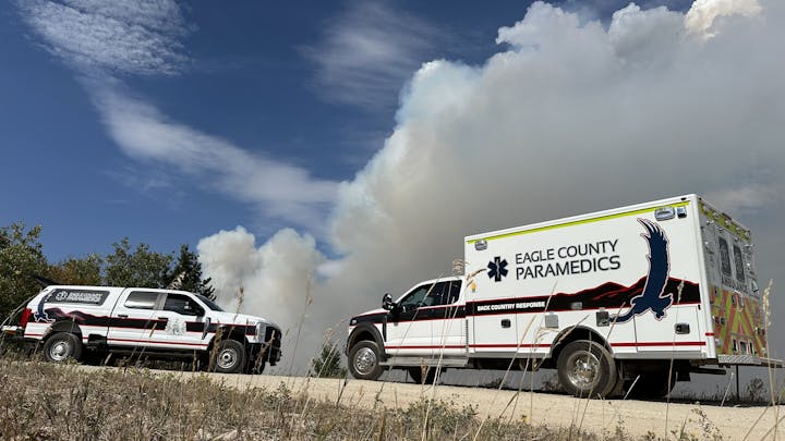 An emergency scene featuring Eagle County paramedic vehicles near smoke rising in the background, indicating potential fire activity.