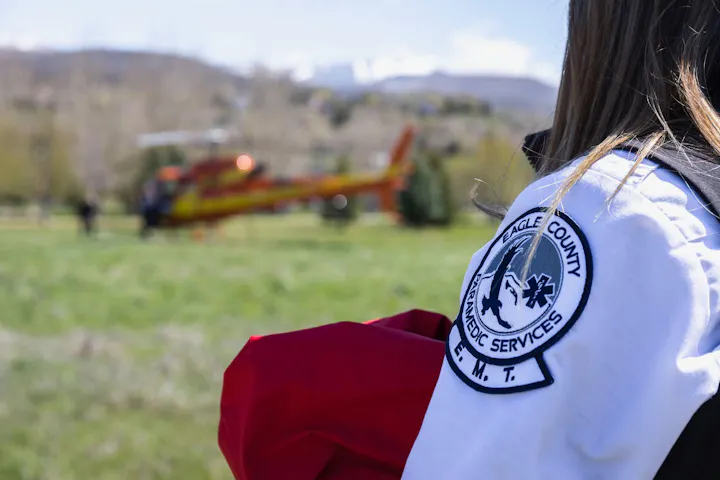 A paramedic in an Eagle County uniform stands near a helicopter, ready for emergency response in a grassy area.