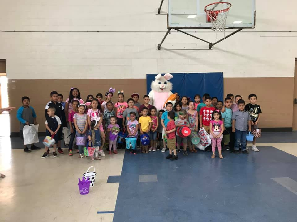 A group of children posing with a person in a bunny costume in a gymnasium.