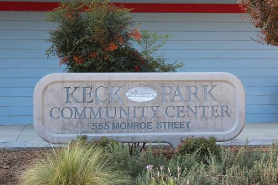 Sign for "Keck Park Community Center" at 555 Monroe Street with shrubs and a red and blue wall behind.