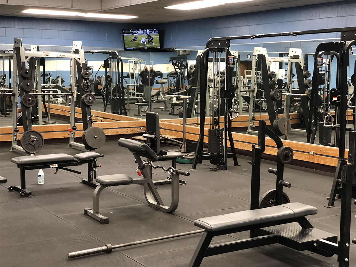 A gym with various workout machines, benches, weights, and a TV showing sports.