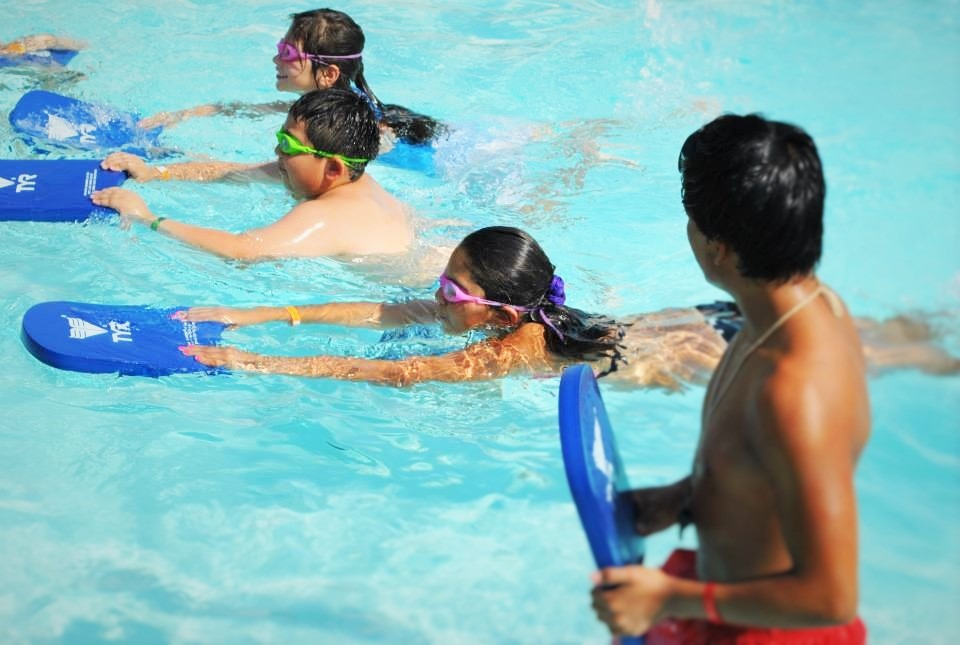 Children in a pool with floatation boards, wearing goggles. Summer fun vibe.