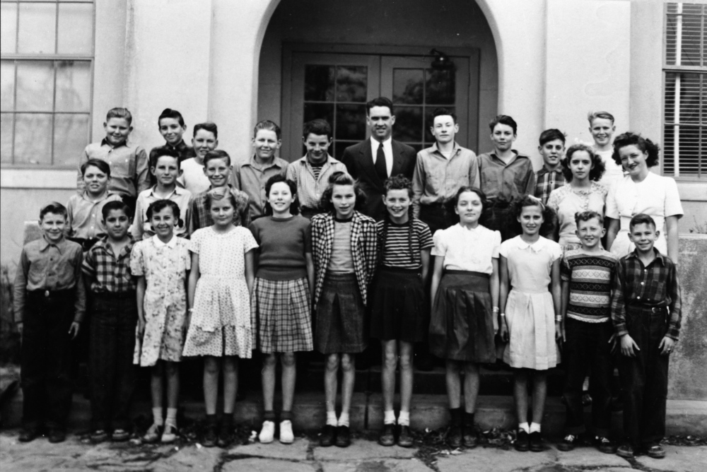 Group of students with their teacher in front of a school building.