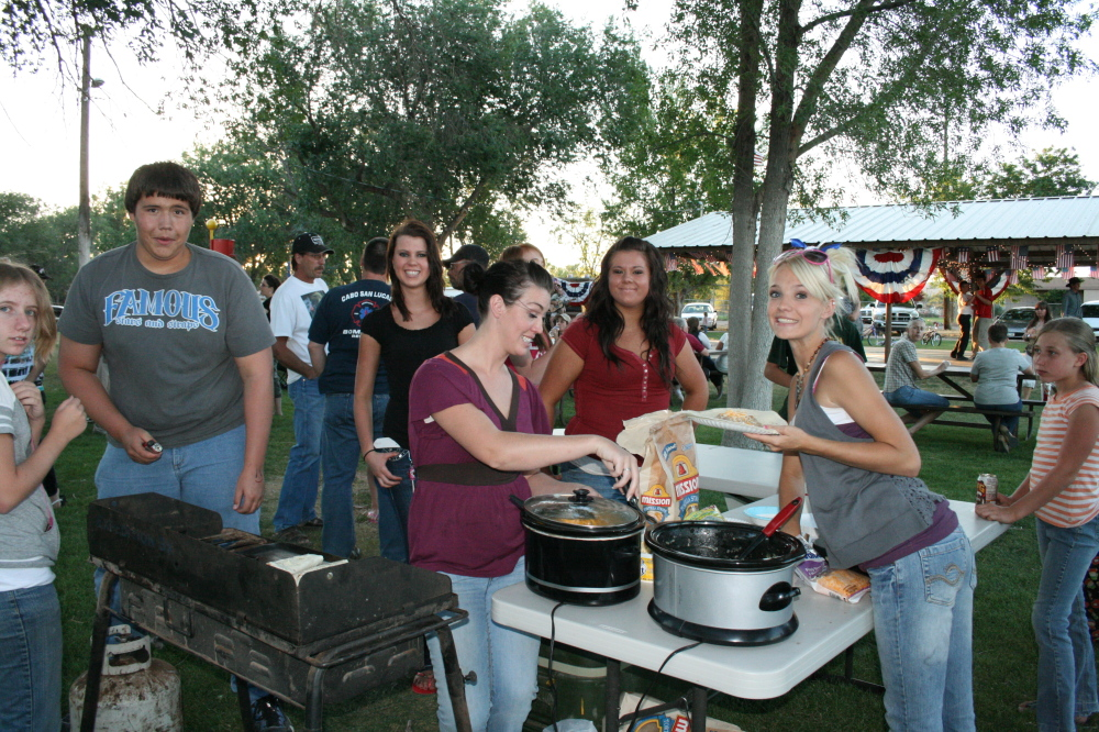 Group of people at an outdoor gathering with food, smiling and interacting near grills and cookers.