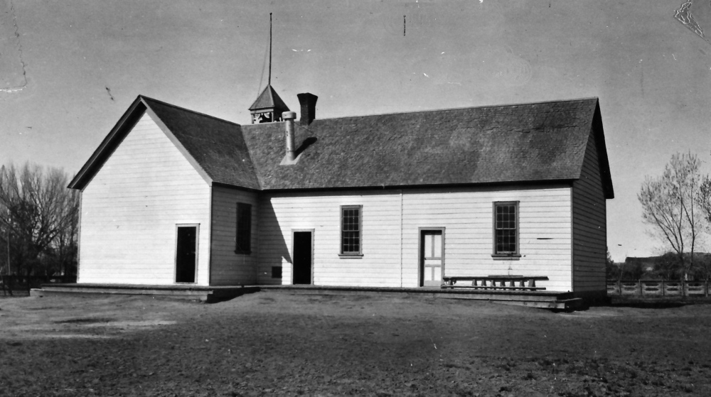 Vintage black-and-white photo of a quaint wooden building, likely a schoolhouse or chapel, with a bell tower.