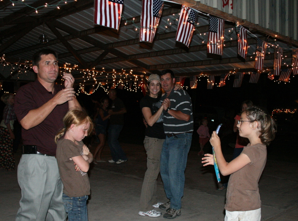 People dancing under a shelter with string lights and American flags, a child with a bottle.