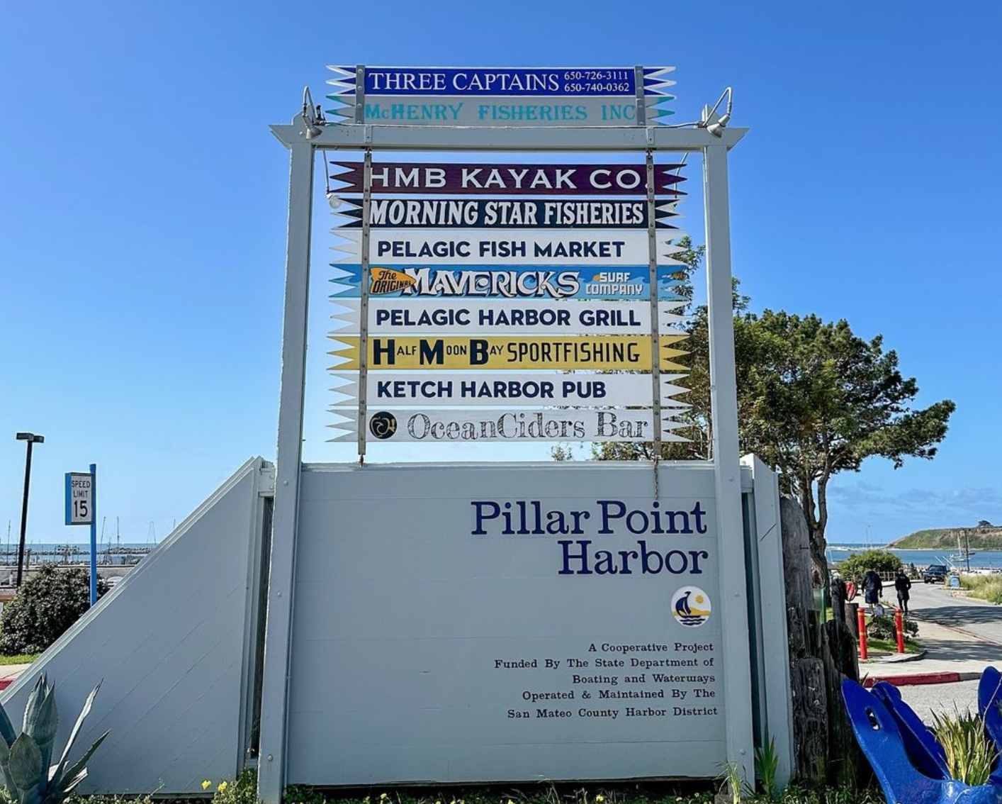 Sign listing businesses at Pillar Point Harbor: kayak rental, fisheries, fish market, surf shop, grill, sportfishing, pub, and cider bar.
