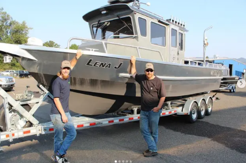 Two people standing by a boat named "Lena J" on a trailer, in an outdoor setting.