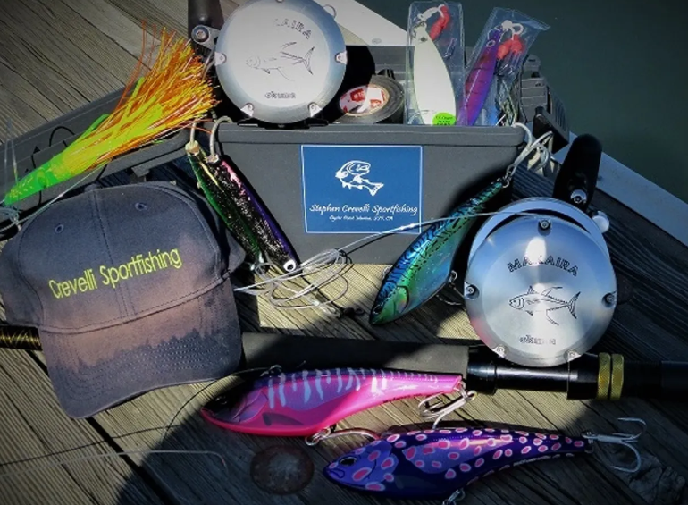 Fishing gear, lures, reels, and a "Crevelli Sportfishing" cap displayed on a wooden surface.