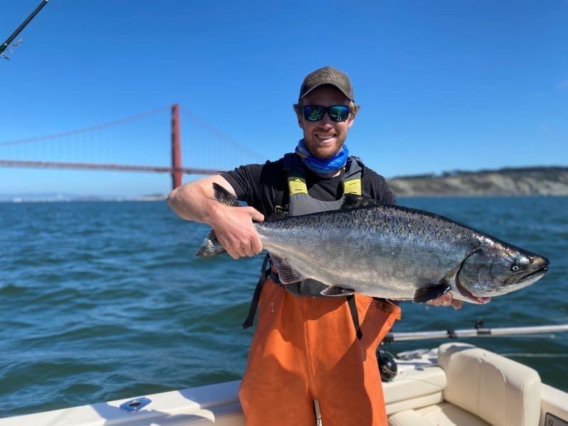 Person on a boat holding a large fish with a bridge in the background.
