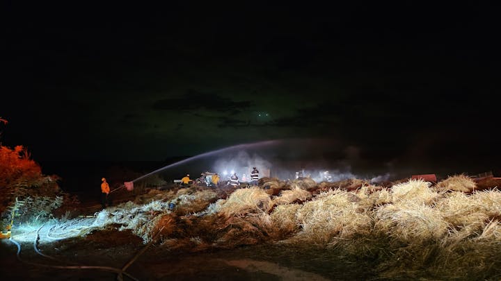 Firefighters dousing a smoldering hay bale pile at night.