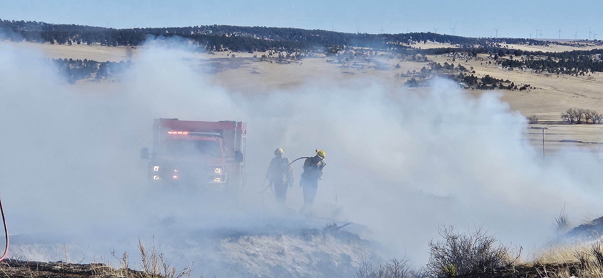 Firefighters and a fire truck in a smoky area, likely battling a wildfire.