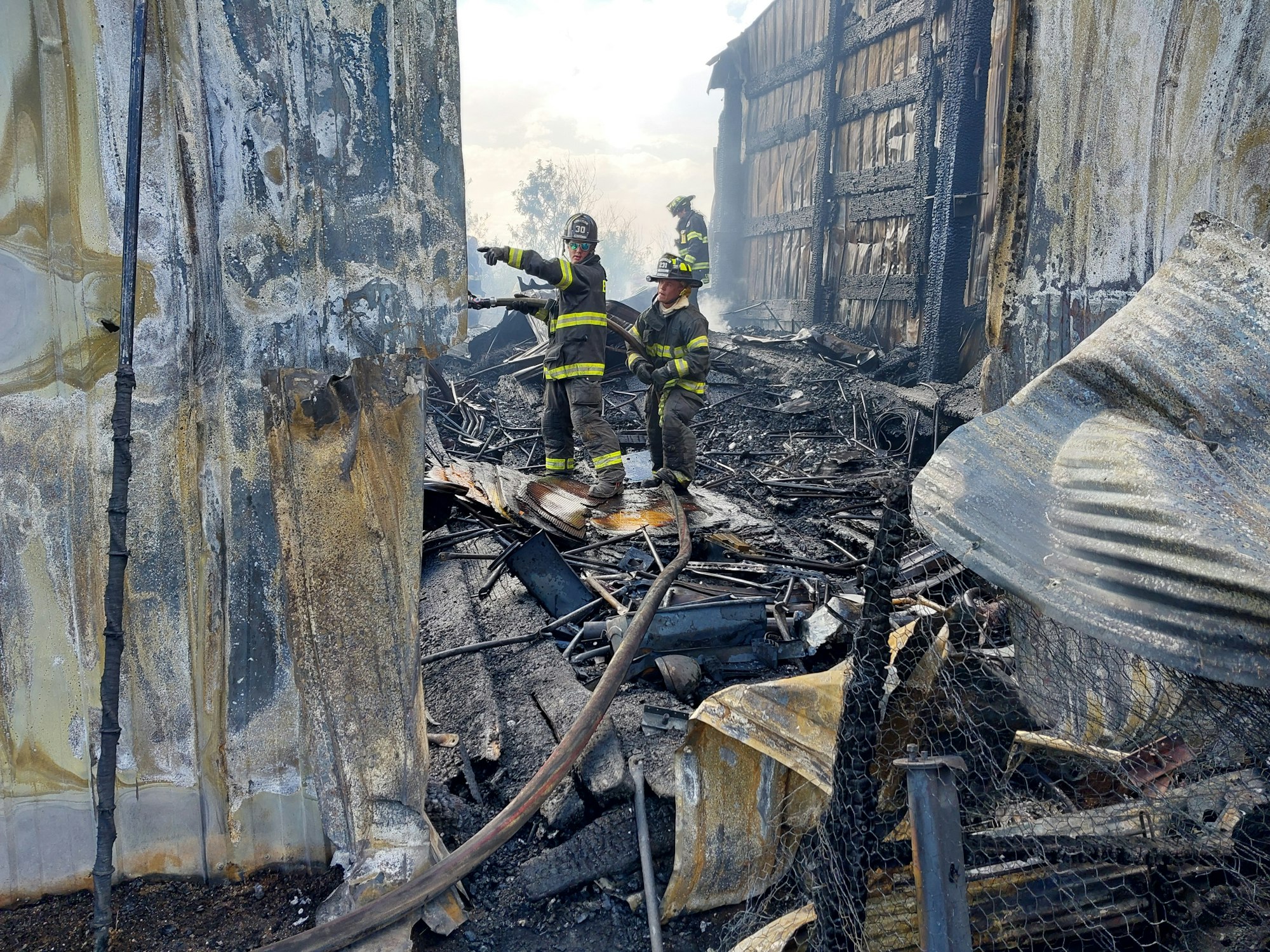 Firefighters amid burnt debris after a fire, with scorched walls and rubble around them.