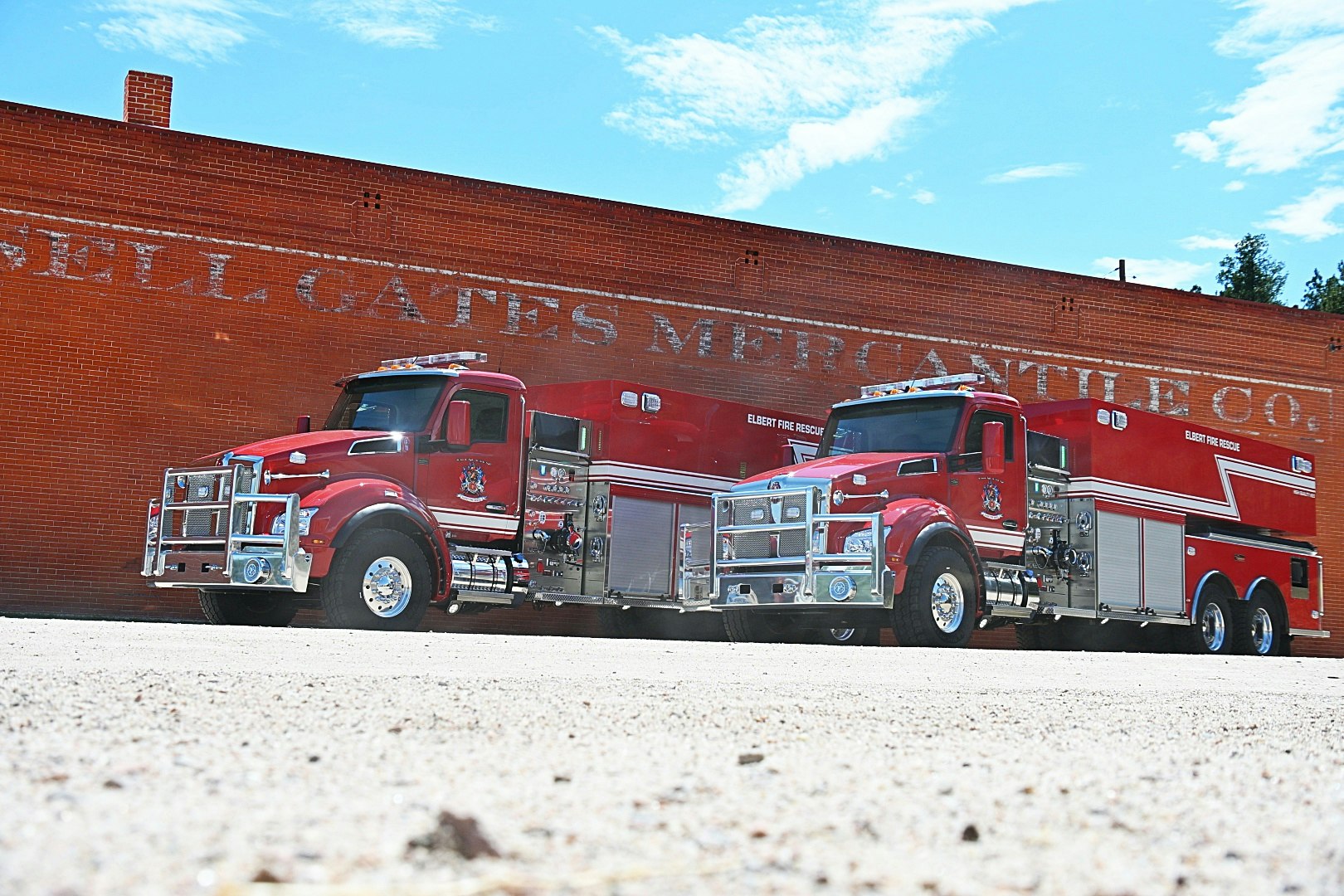 The image features two red fire trucks parked in front of a brick wall with the text "SELL GATES MERCANTILE CO." visible.