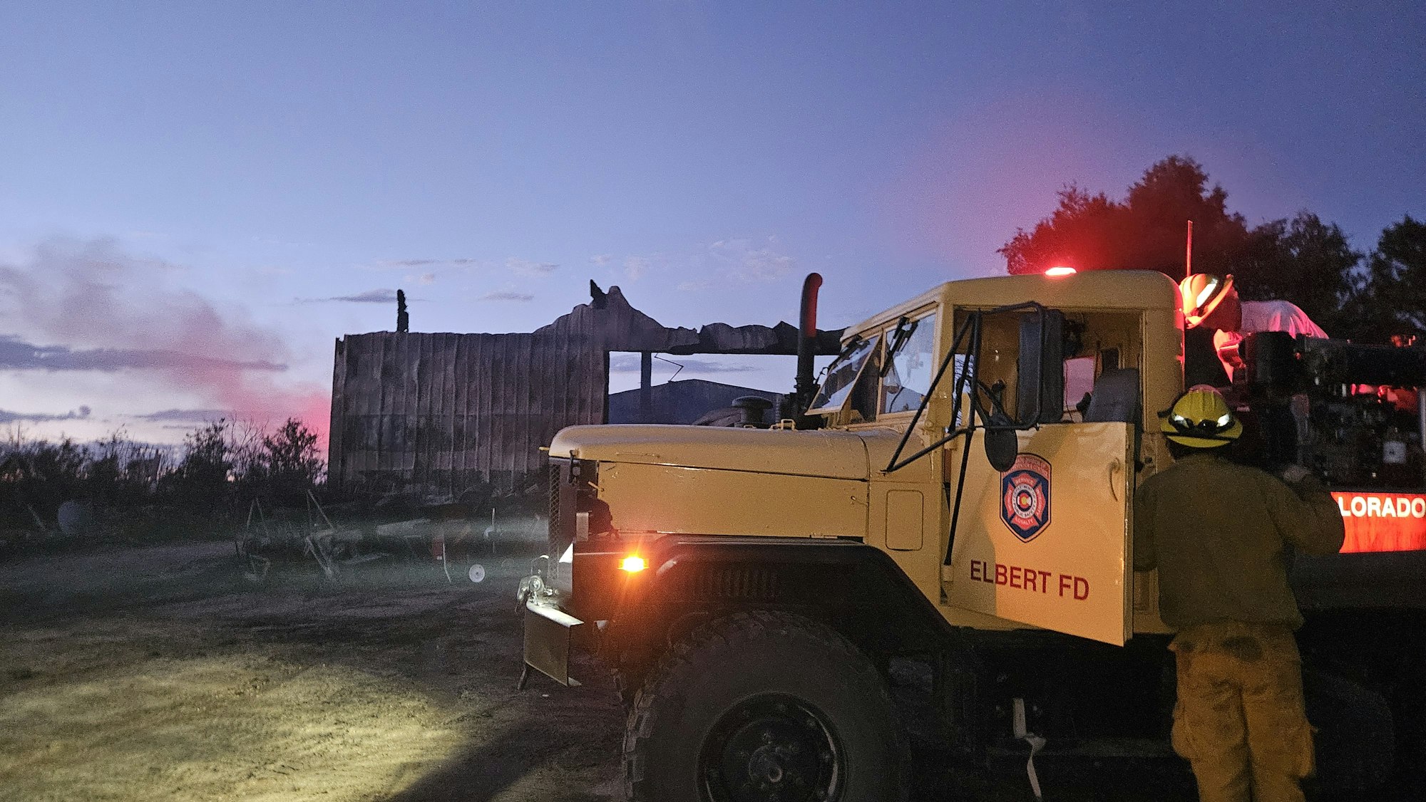 Firefighters beside a truck at dusk with equipment, preparing for action.