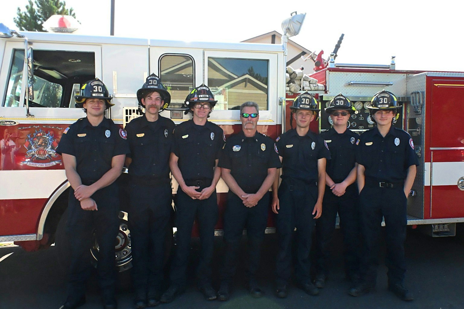 Six firefighters in uniform pose in front of a fire truck.