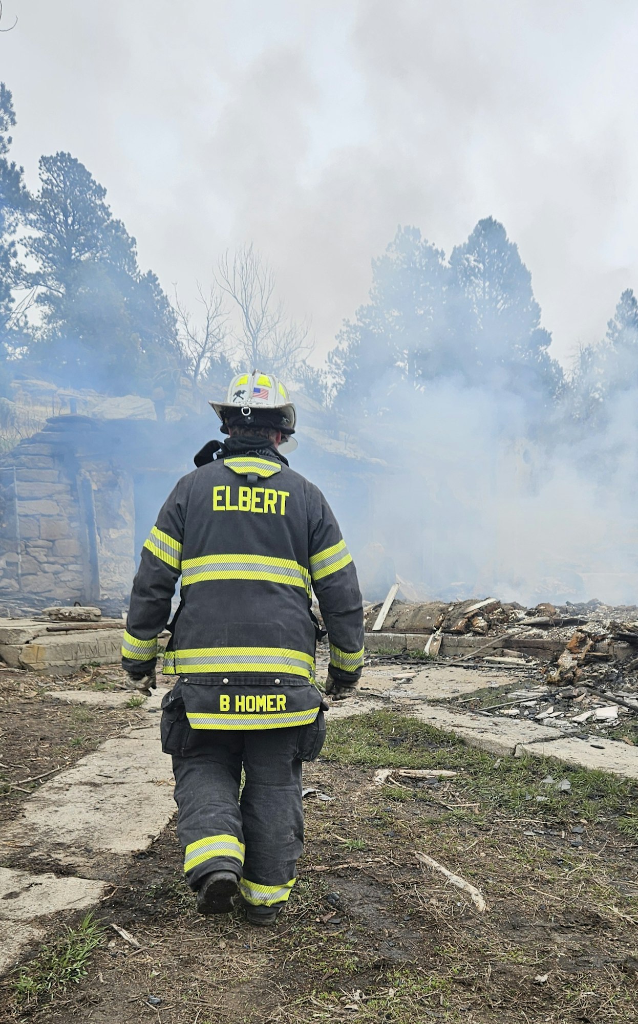 A firefighter facing a smoky area with remnants of destruction, possibly after a fire incident.