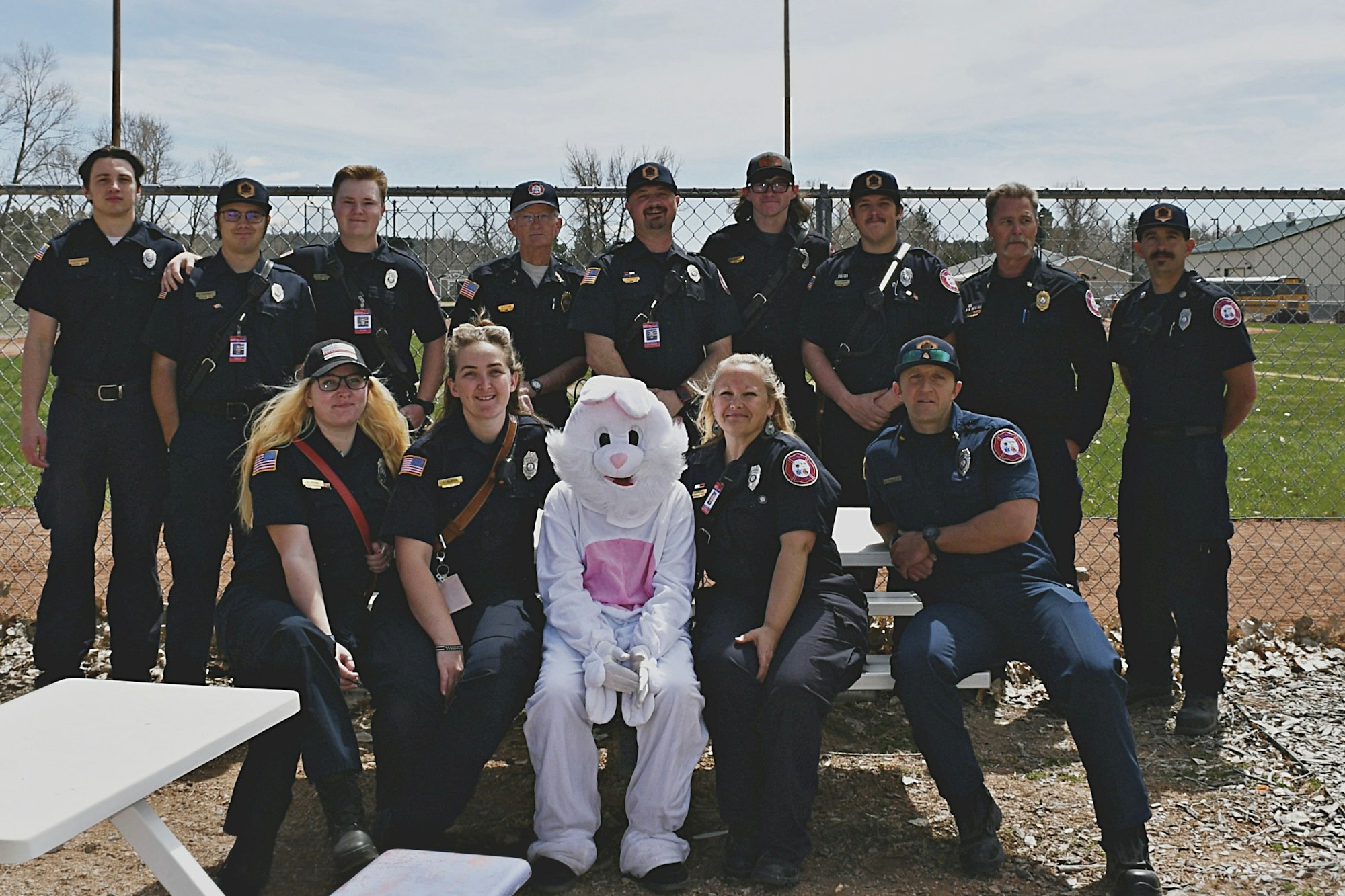 A group of uniformed personnel with an Easter Bunny mascot, posing in front of a fence outdoors.