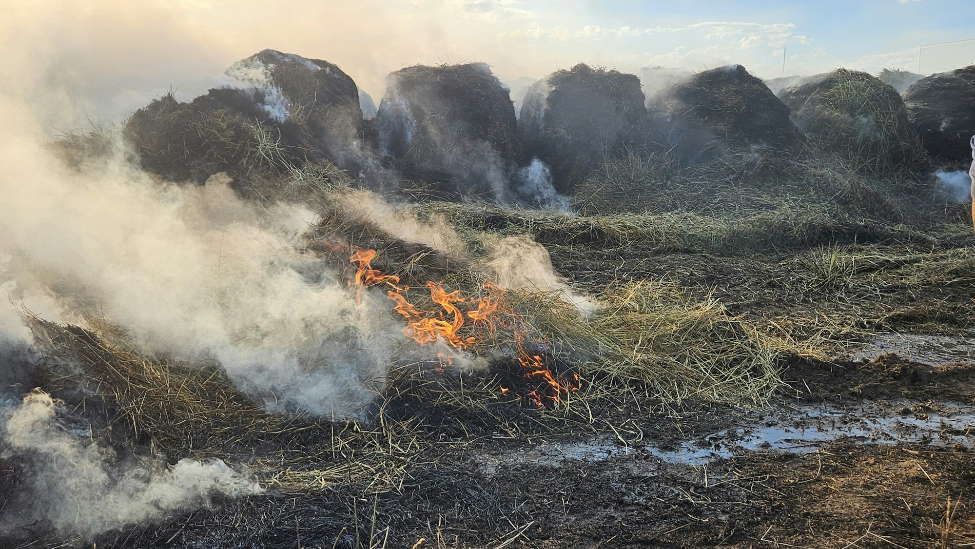 Hay bales smoking and burning in a field with visible flames and smoke.
