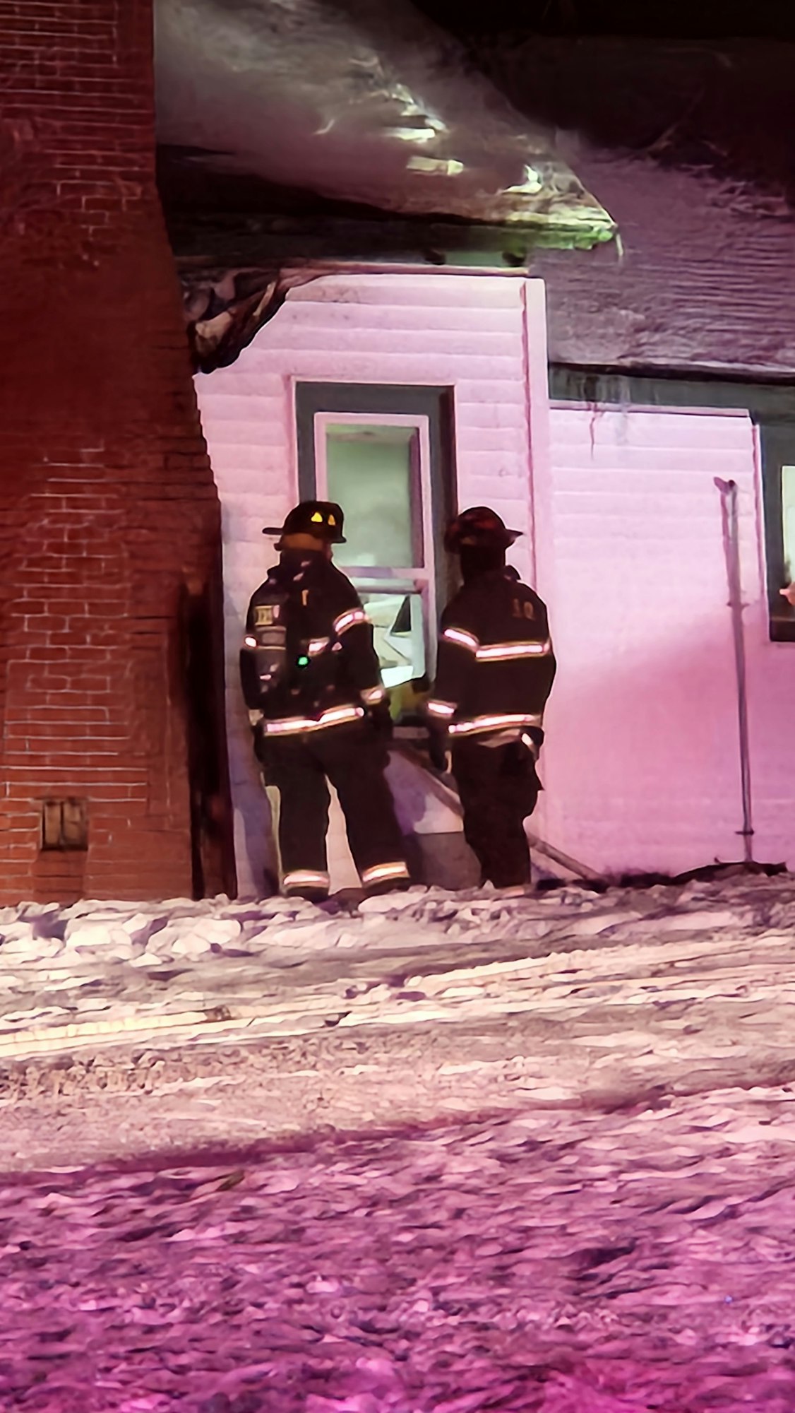 Firefighters standing outside a building at night, with snow on the ground.
