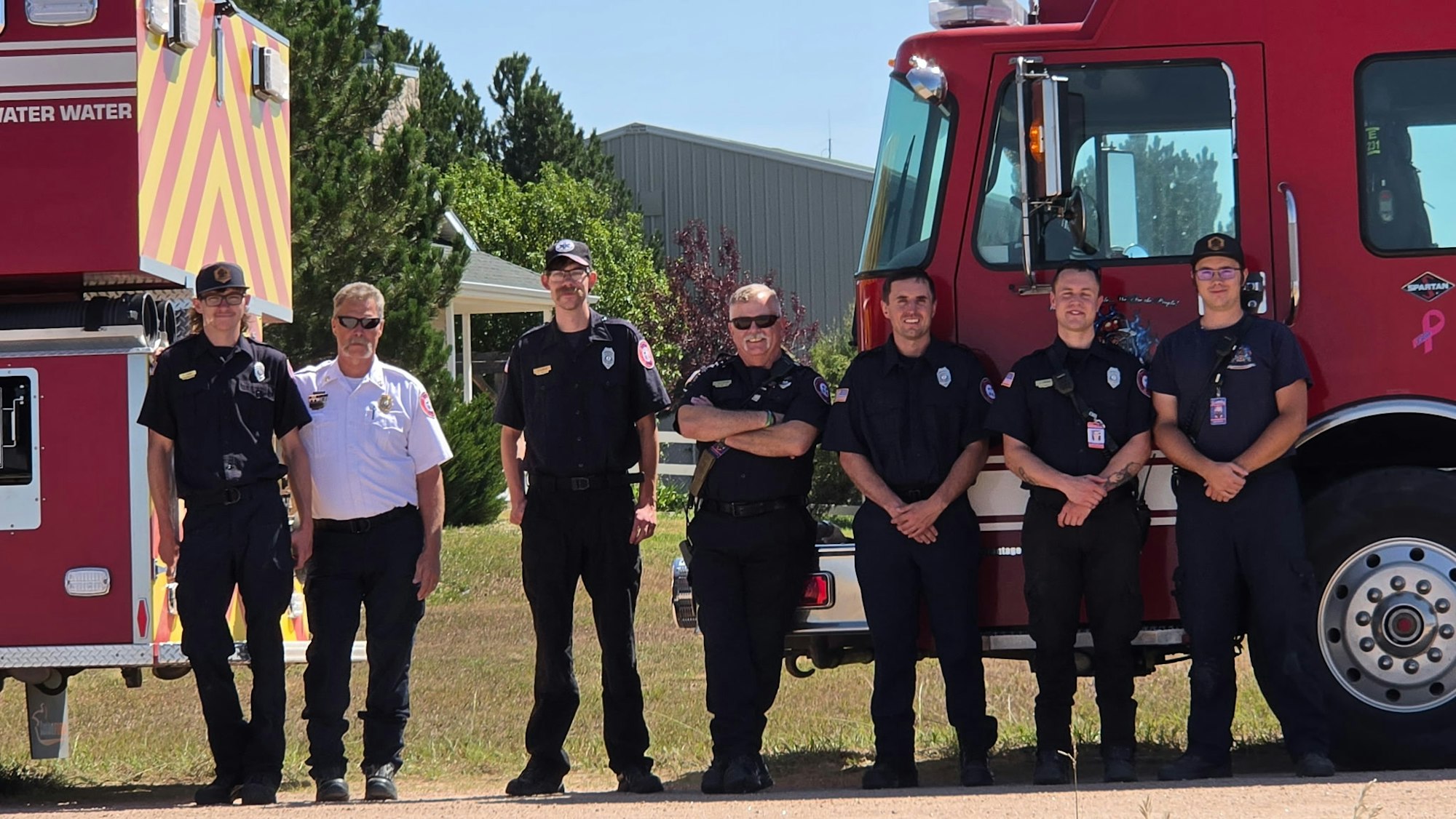 A group of firefighters and officials posed in front of a fire truck on a sunny day.