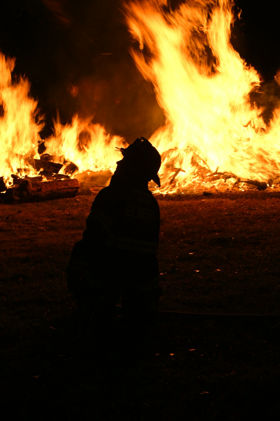 A silhouette of a person near a large, intense fire at night.