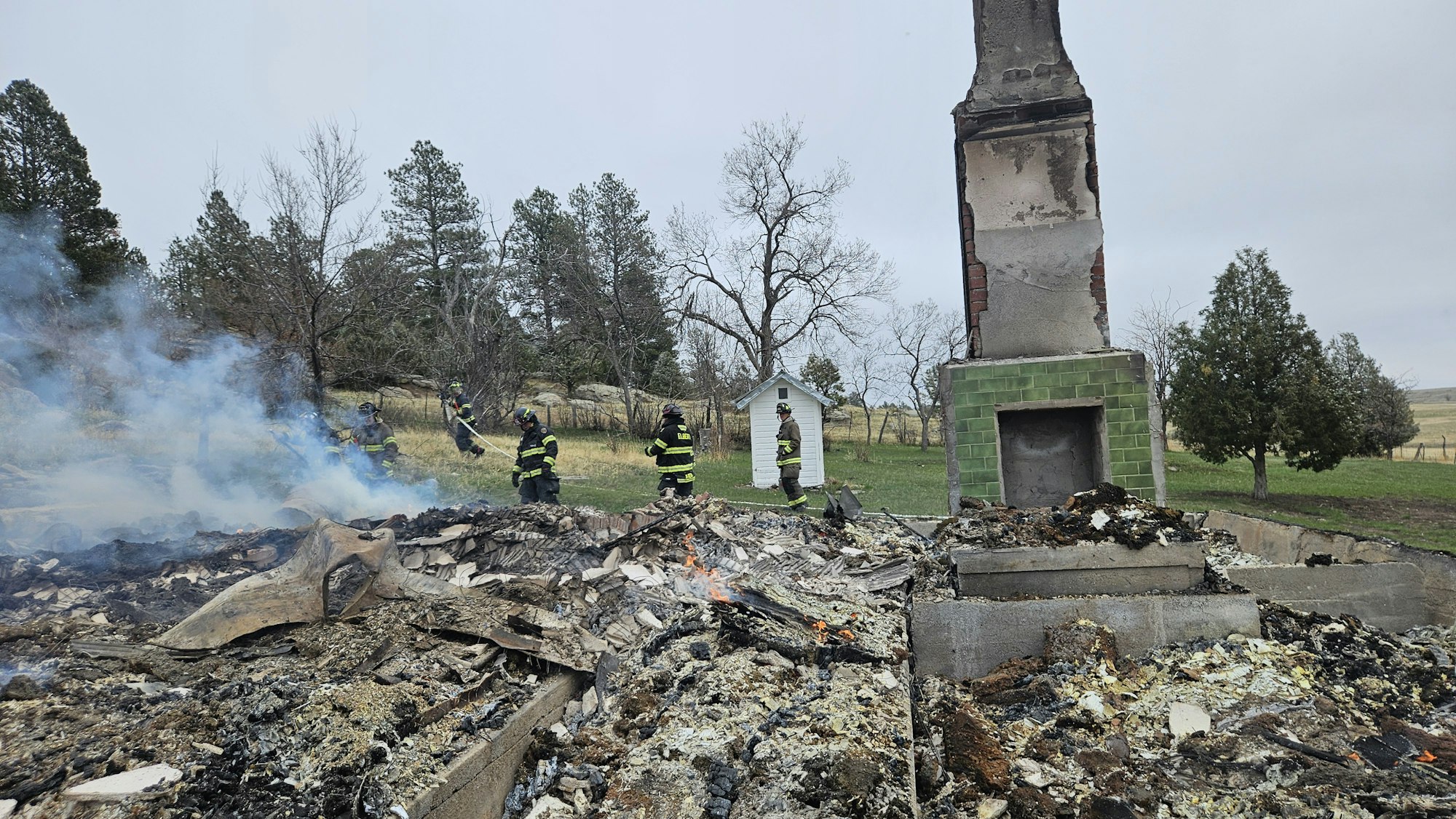 Firefighters at the site of a burned-down building with only a chimney remaining.