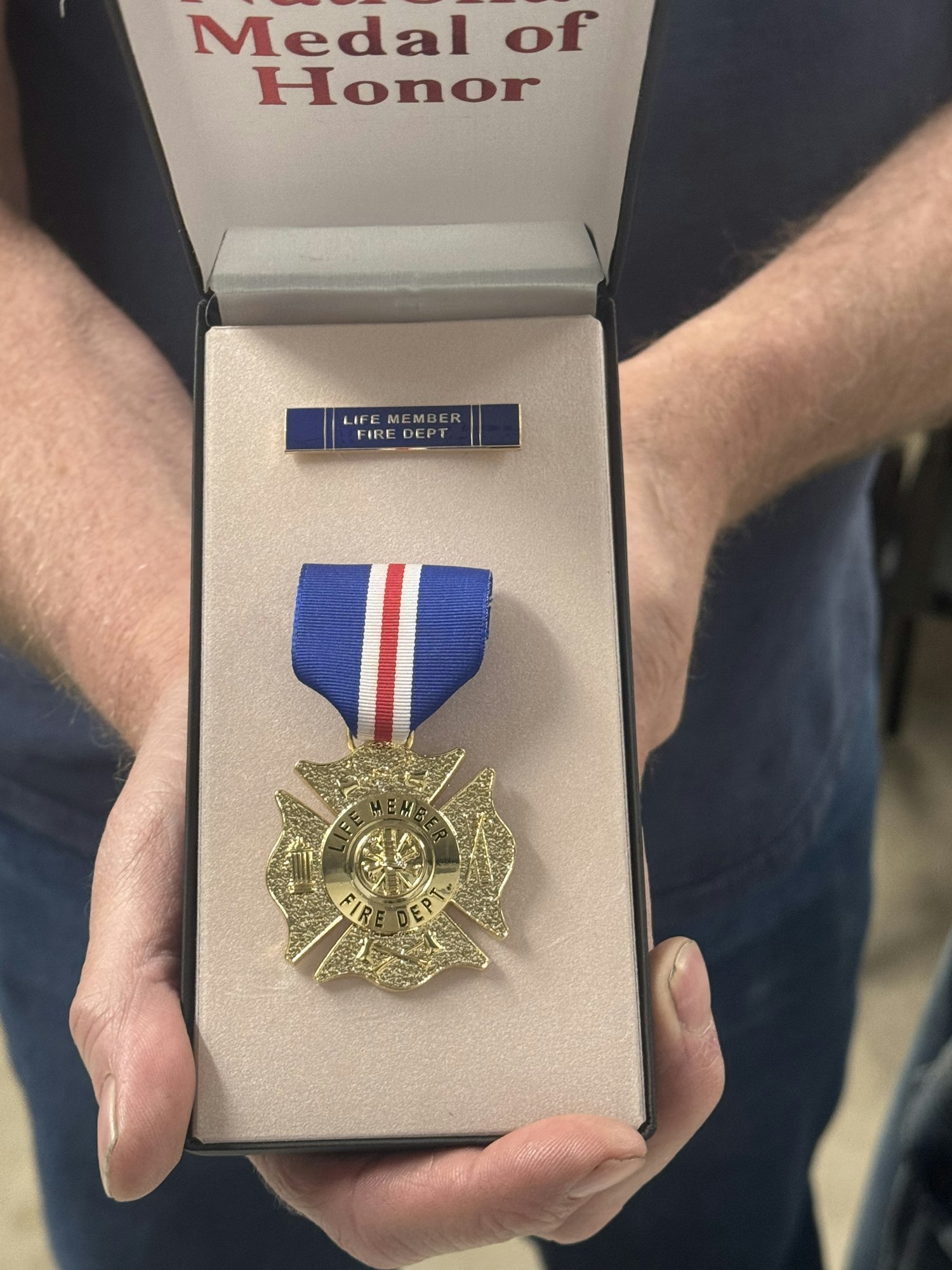 A Medal of Honor display with a "Life Member Fire Dept" badge and a gold firefighter-shaped medal with a blue ribbon.