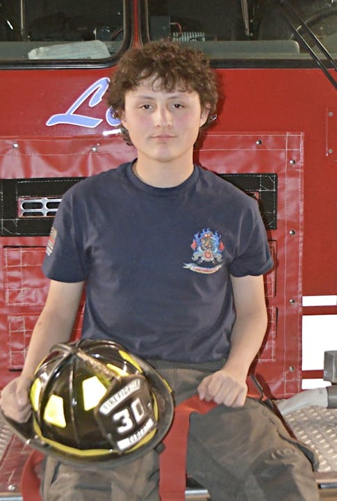 Person sitting in front of a red fire truck holding a firefighter helmet.