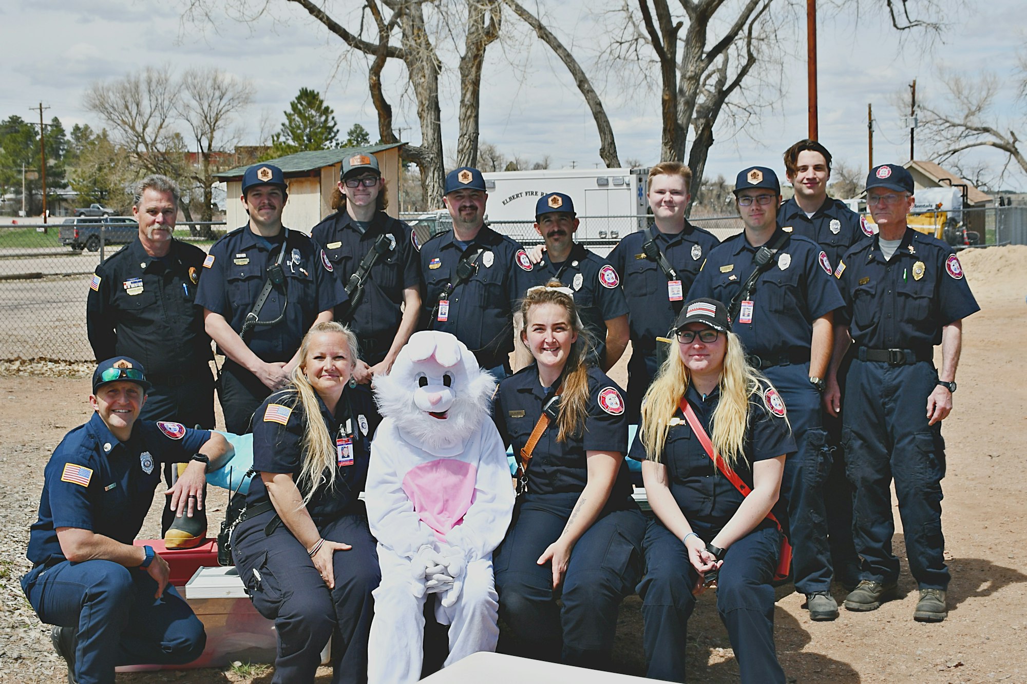 A group of uniformed people posing outdoors with someone in a rabbit costume.