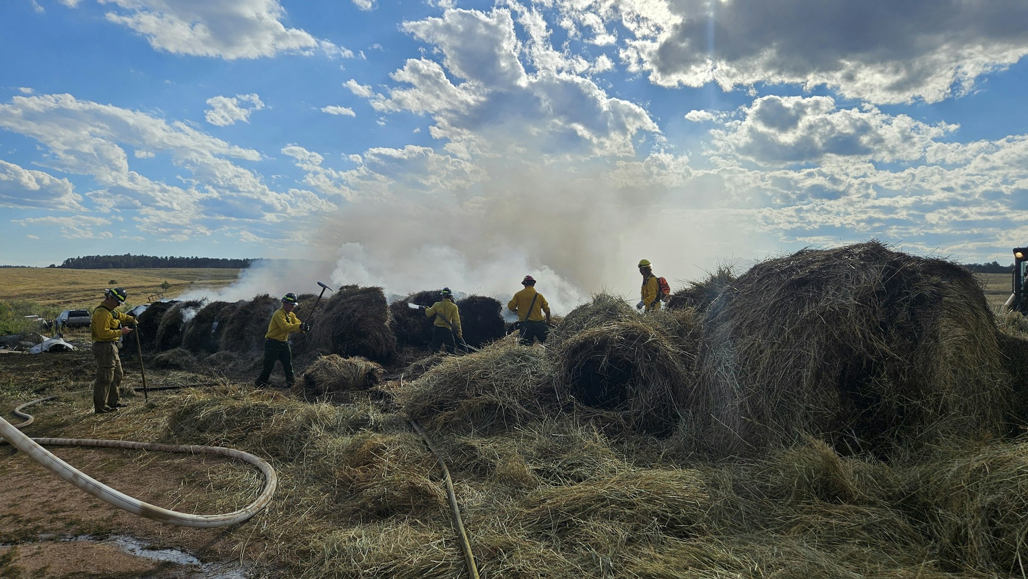 Firefighters tackling a hay bale fire under a cloudy sky.