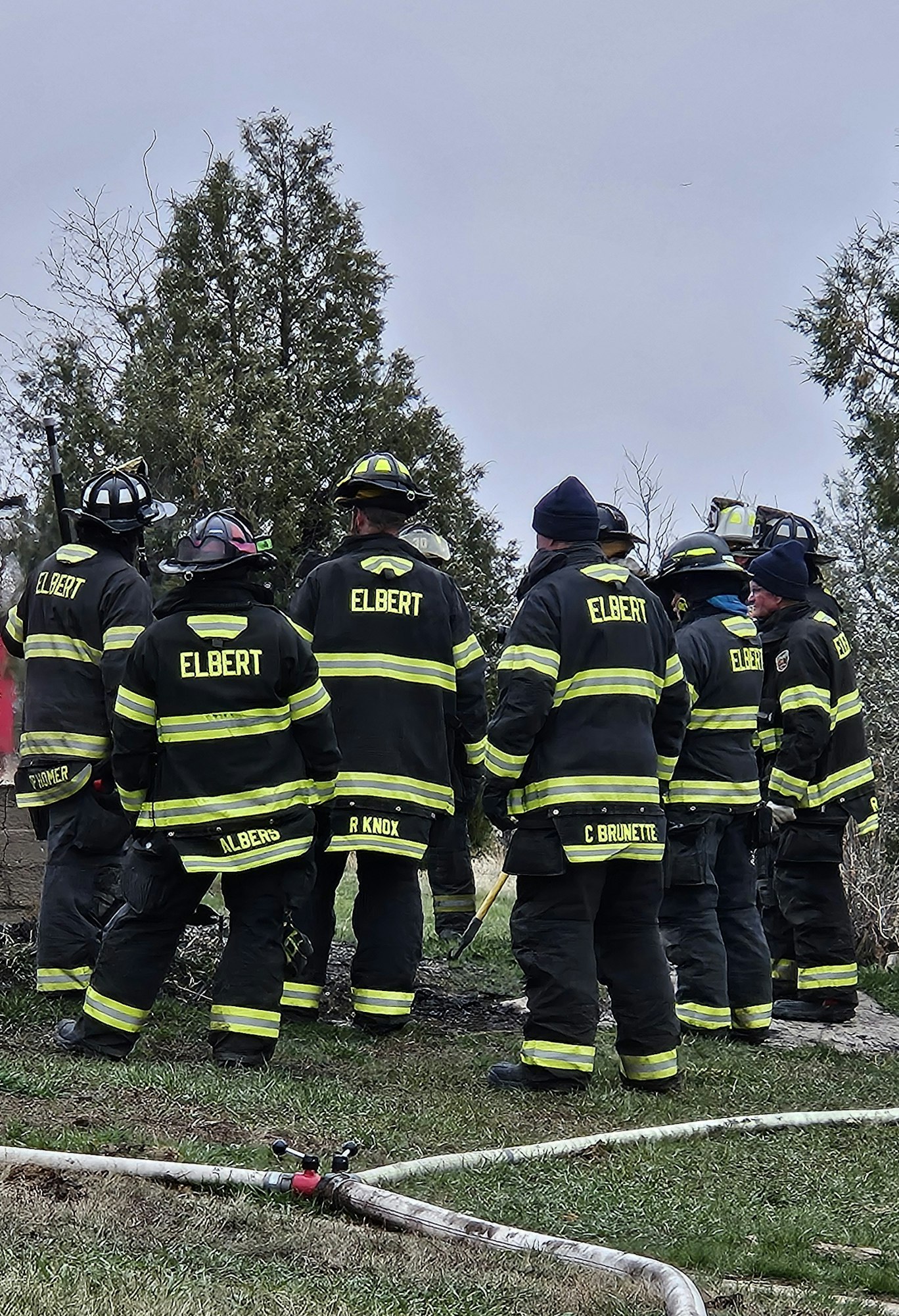 Firefighters in gear standing together outdoors, possibly assessing a situation or receiving instructions.
