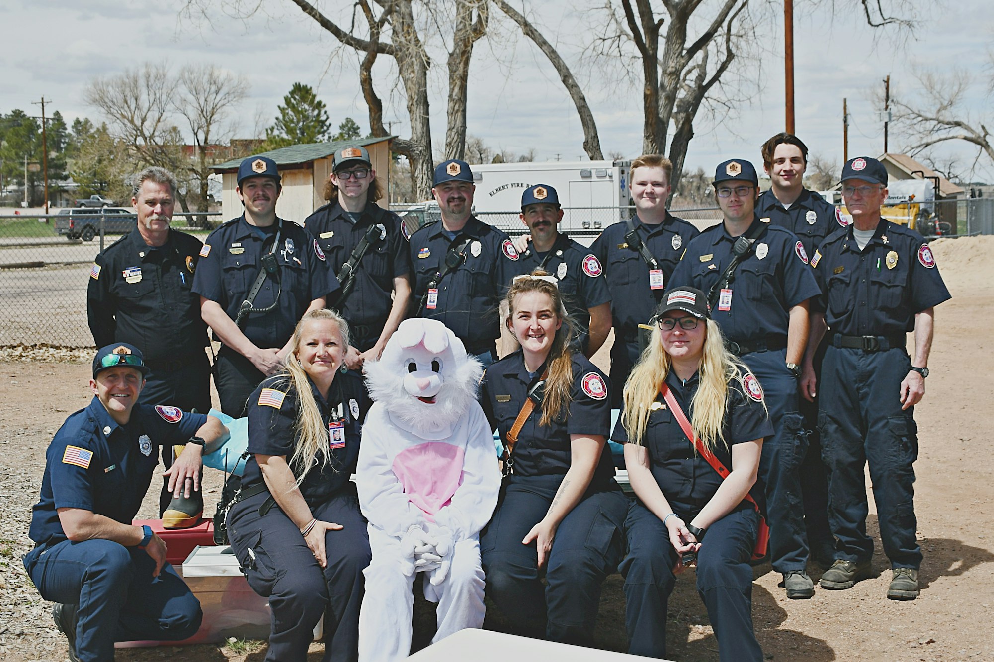 Group of firefighters posing with someone in a bunny costume outdoors.