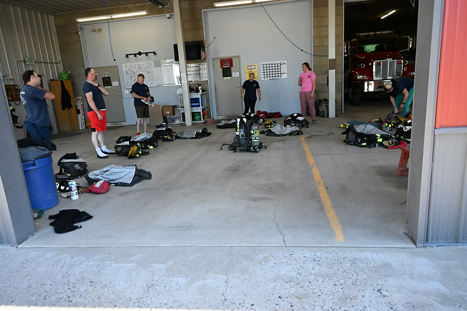 People in a fire station standing around gear and equipment.