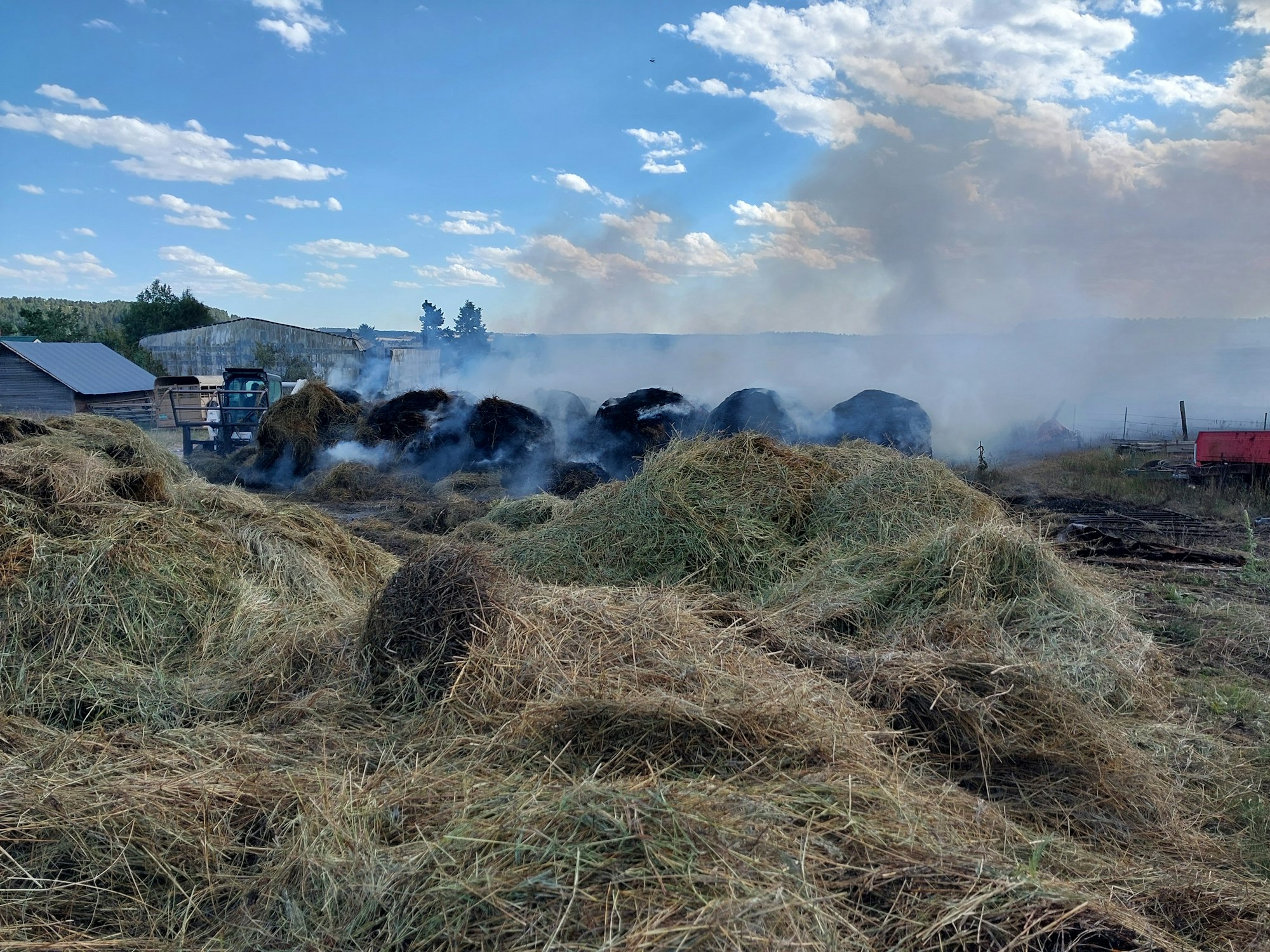Hay bales on fire with smoke rising on a farm.