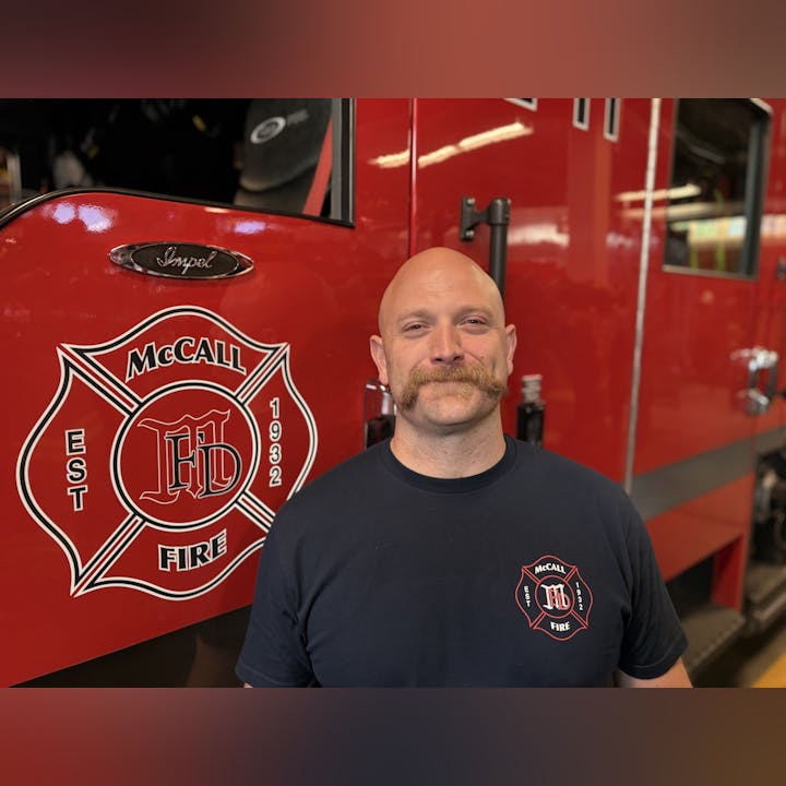 A person stands in front of a fire truck with "McCall Fire" and "Est 1932" logos.