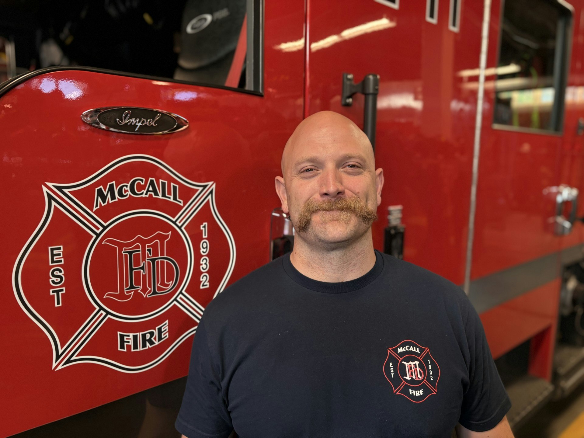 A person stands in front of a fire truck with "McCall Fire" and "Est 1932" logos.